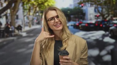 Kahveli bir kadın şehrin caddesinde gülümsüyor. Parlak bir günde çağrı yapıyor. Gözlüklü ve spor ceketli..