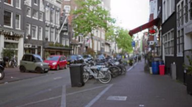 Amsterdam caddesinin bulanık manzarası. Bisikletler, park edilmiş arabalar ve geleneksel binalar. Hollanda 'da kentsel yaşam ve mimari sergileniyor..