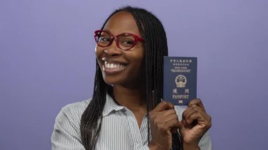 Gözlüklü, gülümseyen ve elinde Hong Kong pasaportu olan bir kadın mor bir arka plana karşı seyahat ve kimlik teması taşıyor..