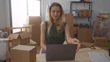 Yeni evdeki yeni oturma odasında, kutuları açılmış, dizüstü bilgisayarını kapatan ve kollarını kavuşturarak tatmin olan genç sarışın bir kadın..