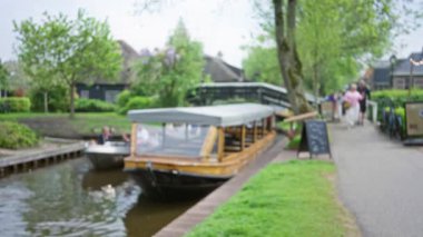 Giethoorn, Hollanda 'daki kanal sahnesinde bulanık tekneler, insanlar ve yemyeşil alanlar huzur dolu su yollarını kaplıyor, kadın ve erkeklerin gezindiği sakin bir bokeh etkisi yakalıyor..