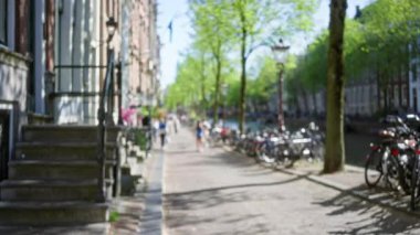 Bisikletler, ağaçlar ve insanların yürüdüğü Amsterdam Kanalı 'nın bulanık manzarası Hollanda' da güneşli bir günün özünü yakalıyor..