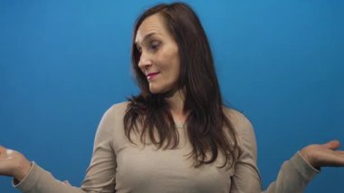 Mavi arka plan duvarına karşı belirsizlikle omuz silken bir kadın gündelik ve karışık bir ifade sergiliyor..