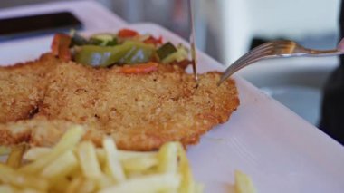 Kadının kapalı bir Akdeniz restoranında sebzeli şnitzel ve patates dilimleyip beyaz bir tabakta lezzetli bir yemeği ön plana çıkardığı yakın plan..