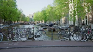 Güneşli bir günde Amsterdam 'ın manzaralı şehir manzarasında bir kanal boyunca uzanan bulanık bisikletler, Hollanda' da canlı bir şehir atmosferi ve huzurlu bir yaşam tarzı yakalıyor..