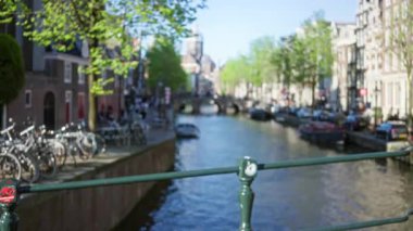 Amsterdam Kanalı 'nın bulanık görüntüsü. Su kenarında bisikletler ve güneşli bir günde arka planda tarihi binalar..
