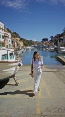 Cala Figür Limanı 'nda gülümseyen bir kadın, Akdeniz boyunca güneşli bir gökyüzünün altına yanaşmış tekneli Mallorca, sakin bir sahil atmosferi yaratıyor..
