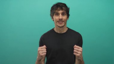 Yumruklarını sıkmış ve gülümseyen genç bir adam stüdyo duvarının önünde kutlama yapıyor..