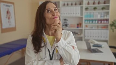 Steteskoplu beyaz laboratuar önlüklü İspanyol kadın doktor klinikte parmak hareketiyle çeneye dokunuyor..