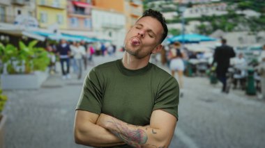 Şehir sokaklarında genç bir adam, canlı bir şehir arka planında mutluluk ve oyunculuğu ifade ederken dövmeleri ve kolları çaprazlanmış bir şekilde güvenle poz veriyor..