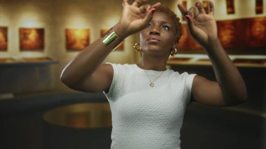 Kadın, müze sergisinde duvardaki çerçeveli tablolara hayranlıkla bakarken inşaat galerisinde el kaldırıyor..