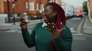 Kadın şehir sokaklarında Amerikan dolarlarıyla dolu cam kavanoz tutuyor, neşe saçıyor, şehir ortamında finansal konsept sergiliyor..