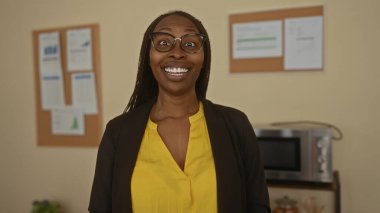 Ofiste gülümseyen bir kadın, sarı bluz ve gözlük takıyor, neşeli tavırları olan olumlu profesyonel titreşimler yayıyor..