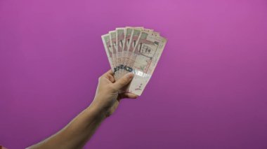 Suudi Arabistan riyal paralarını izole edilmiş mor arka plan duvarına karşı tutan adam, canlı ve minimalist bir ortamda para ve finans gösteriyor..