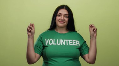 Yeşil gönüllü gömleğiyle poz veren bir kadın canlı sarı bir arka plana karşı, pozitifliği ve barış işaretleriyle güçlenmeyi ifade ediyor..