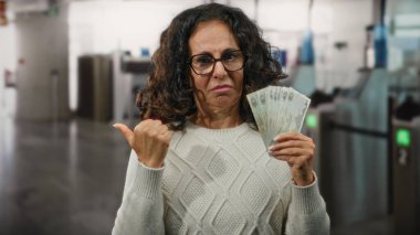 Havaalanı terminalinde elinde Dirham banknotları tutan bir kadın sorgulama ifadesi gösteriyor..