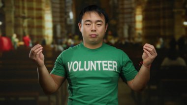 Yeşil gönüllü tişörtü giyen genç adam kilisenin arka planında güvenle duruyor..