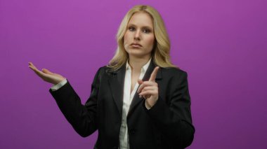 Bir kadın tek eliyle hareketler yapıyor. Durma sinyaliyle canlı mor bir arka plana karşı, dışavurumsal iletişim sergiliyor..