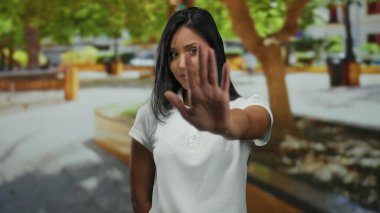 Parkta el işaretleriyle duran genç bir kadın. Çevresi canlı yeşil ağaçlarla çevrili. Kendine güveni ve kendine güveni var..