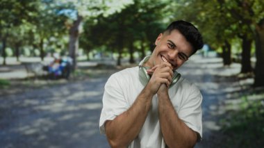 Yeşil ağaçlarla çevrili bir parkta kulaklık takan gülümseyen bir adam açık havada neşeli bir portre çiziyor. Canlı, doğal bir ışıkla çekiliyor.