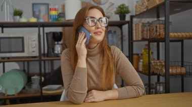 Ofiste telefonla konuşan bir kadın, raflar, mikrodalga fırın, bardaklar görünür, gözlük, süveter, kızıl saçlı, genç, yetişkin, kapalı alan ayarlı, modern bir iş yeri sergiliyor..