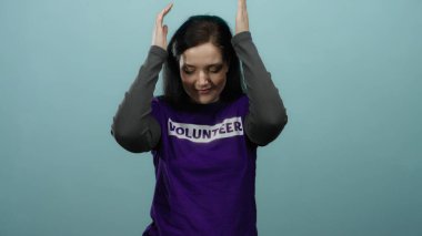 Mavi arka planda mor bir gönüllü tişörtle dans eden kadın gözleri kapalı ve elleri havada mutluluk ve coşkuyu ifade ediyor..