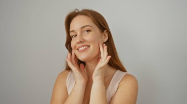 Elleri yanaklarında gülümseyen bir kadın beyaz bir arka planda izole edilmiş genç ve çekici bir kızıl saçlıyı güzelliğini gösterirken yakalar..