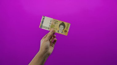 Güney Kore 'yi elinde tutan adam canlı bir mor arka plana karşı banknot kazandı ve para biriminin kendine özgü tasarımı ve kültürel önemini vurguladı..