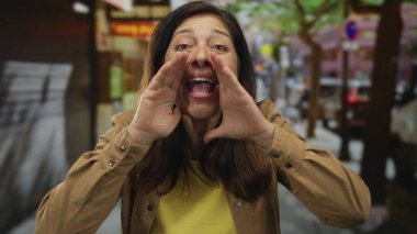 Orta yaşlı İspanyol bir kadın sokakta elleri sımsıkı bağlı bağırıyor; coşkulu bir ses ifadesi var..