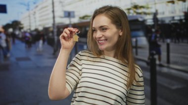 Yoğun şehir caddesinde ev anahtarlığı ve parlak bir gülümseme tutan genç kadın, ev sahipliği mutluluğu.