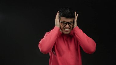 Gözlüklü, kırmızı kazaklı genç adam siyah bir arka plana karşı başı dertte, hayal kırıklığı ve gerilim taşıyor..