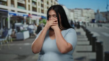 Şehir sokaklarında gülen bir kadın modern kentsel bir arka planda, gündelik giysiler giyiyor, elleri ağzında neşe ve duyguyu ifade ediyor..