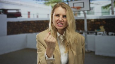 Açık hava basketbol sahasında kızgınlığını ifade eden kadın, beklenmeyen bir atletizm ortamında yakalanan duygu ve kararlılığı vurguluyor.