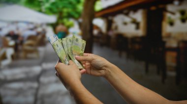 Şili pesolarını şehir sokaklarında tutan, hareketli bir şehir ortamında banknotlar sergileyen, açık hava iş yatırımlarını yansıtan bir adam..