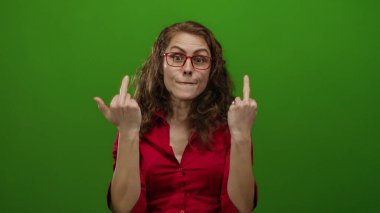 Gözlüklü kadın, parlak yeşil arka plana karşı kaba bir el hareketi yapıyor. Parlak kırmızı tişörtle meydan okuma ve duyguyu tasvir eden cesur bir ifadeyle..