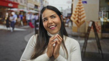 Kendine güveni tam bir kadın, neşeli bir caddede entrika çevirirken ellerini bir araya getiriyor. Genç Latin bir şahsiyet açık havada muzip, gülümseyen bir ifadeyle duruyor..