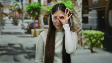 Şehir caddesinde gün ışığında şehir yeşillikleriyle çevrili neşeli bir jest yapan kadın, neşe ve güveni dile getiriyor..