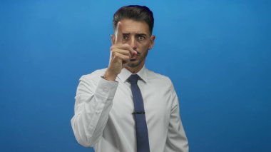 Resmi gömlekli ve kravatlı genç adam stüdyoda görülmemiş bir nesneyi işaret ediyor mavi bir duvara odaklanmış bakışla; dikkat odaklanma azmi.