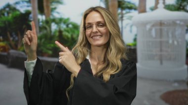 Kadın parkta yargıçlık yapıyor ve gülümsüyor. Siyah üniforma giyiyor ve yeşil ağaçların arasında gözlük takıyor. Bu da liderlik ve otoriteyi gösteriyor..