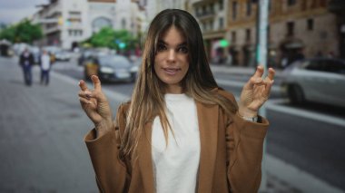 İspanyol kadın bulutlu gökyüzünün altında günlük kıyafetler giyerek işlek şehir caddesinde tırnak işareti yapıyor..