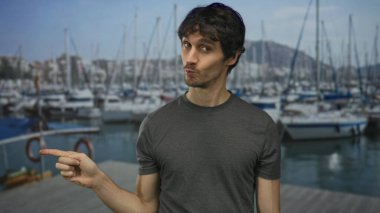 Gri gömlekli adam güneşli bir öğleden sonra güneşli bir gökyüzünün altında modern bir binanın dışındaki tekneleri işaret ediyor..