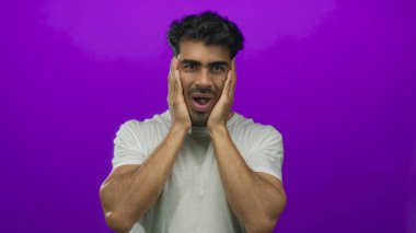 Beyaz tişörtlü genç İspanyol adam, gergin omuzları ve gergin kaşları olan mor stüdyodaki tapınakları kavrıyor; stres gerilimi.