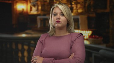 Süslü kilise içinde kolları bağlı genç sarışın kadın mihrapta parlayan mumlarla duruyor; reddedilme.