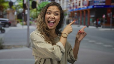 Şehirli sokak ortamını coşkuyla işaret eden kadın, dışardaki dinamik çevreyi işaret eden hareketli şehir arkaplanı ile dışa dönük duygular ve gündelik tarzını sergiliyor..
