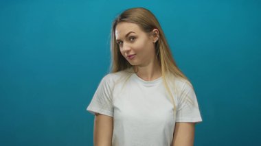 İzole edilmiş mavi bir arka plana karşı duran kadın, düşünceli bir ifadeyle, basit beyaz tişörtle gençliği ve gündelik tarzını vurgulayarak, modern zarafeti iletiyor..