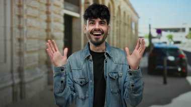 Kot ceket giyen genç adam, coşkulu bir şekilde gülümsüyor ve şehrin hareketli sokaklarında elleri havada geziyor..