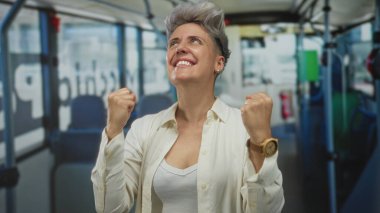 Kısa saçlı bir kadın, parlak ışıklı otobüs içinde yumruklarını sıkar ve sırıtır. Zafer..