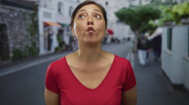 Kadın dudaklarını büzüyor ve başını hafifçe eğiyor. Sıcak güneş ışığı altında şehir caddesinde dururken ıslık çalıyormuş gibi..