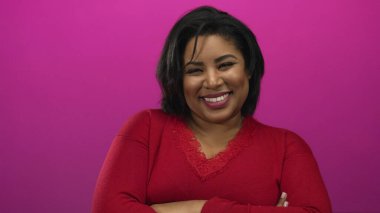 Çapraz kolları ve kendine güveni olan Latin bir kadın canlı pembe bir duvara karşı duruyor, kırmızı bir kazak giyiyor, kendine güveni ve pozitifliği somutlaştırıyor..