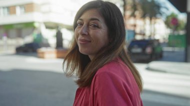 Şehir caddesinde park halindeki arabanın yanında yüzü gülen bir kadın ifadesini aydınlatan yumuşak güneş ışığıyla; memnuniyet.